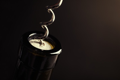 Photo of Opening bottle of wine with corkscrew on dark background, closeup