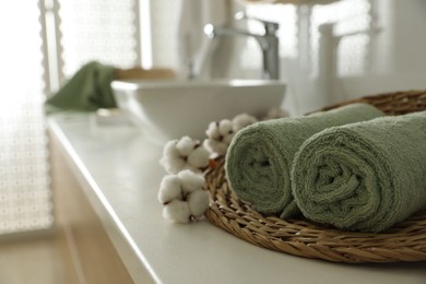 Wicker tray with clean towels and cotton flowers on countertop in bathroom. Space for text