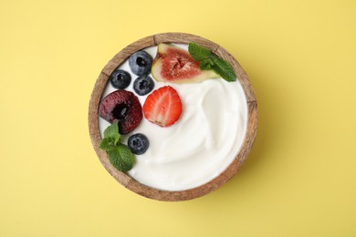 Photo of Bowl with yogurt, berries, fruits and mint on yellow background, top view