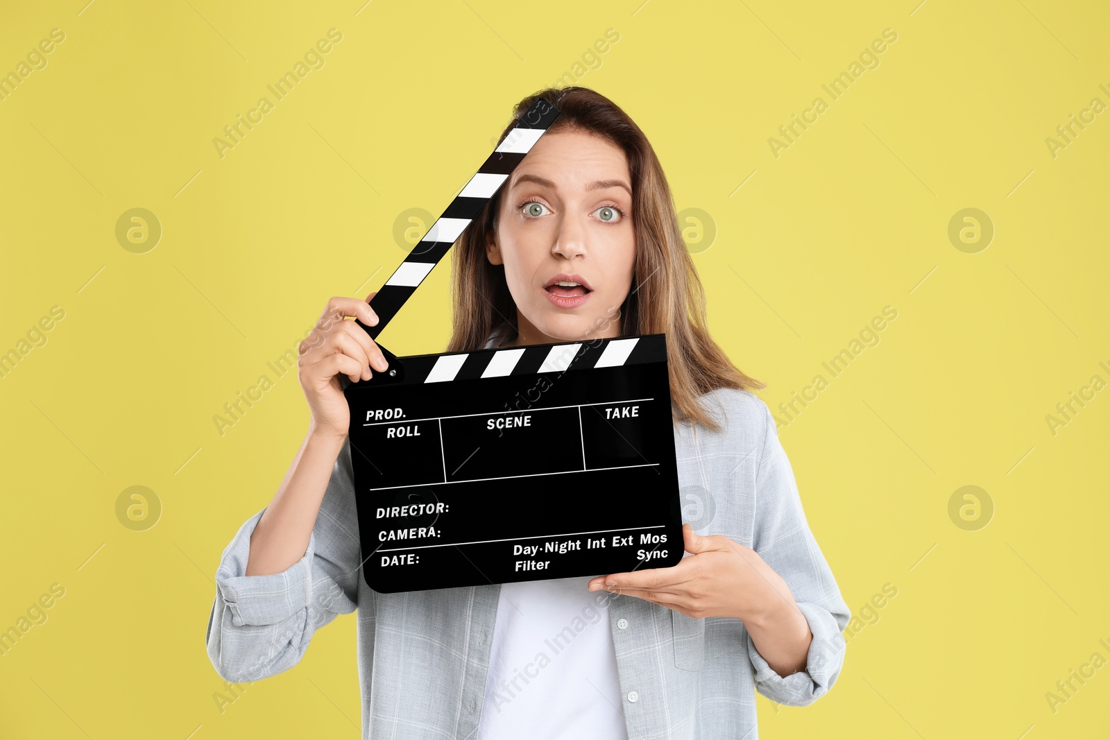 Photo of Making movie. Beautiful surprised woman with clapperboard on yellow background