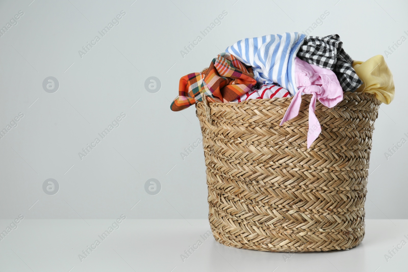 Photo of Wicker laundry basket with different clothes on light background. Space for text