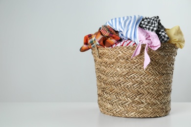 Wicker laundry basket with different clothes on light background. Space for text