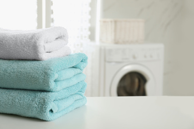 Photo of Stack of clean towels on table in laundry room. Space for text