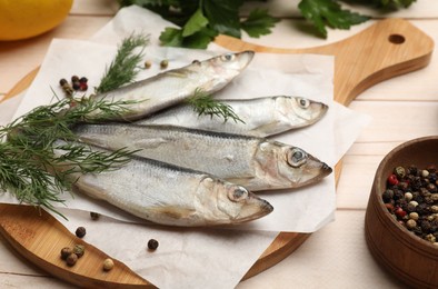 Photo of Fresh raw sprats, peppercorns and dill on light wooden table, closeup