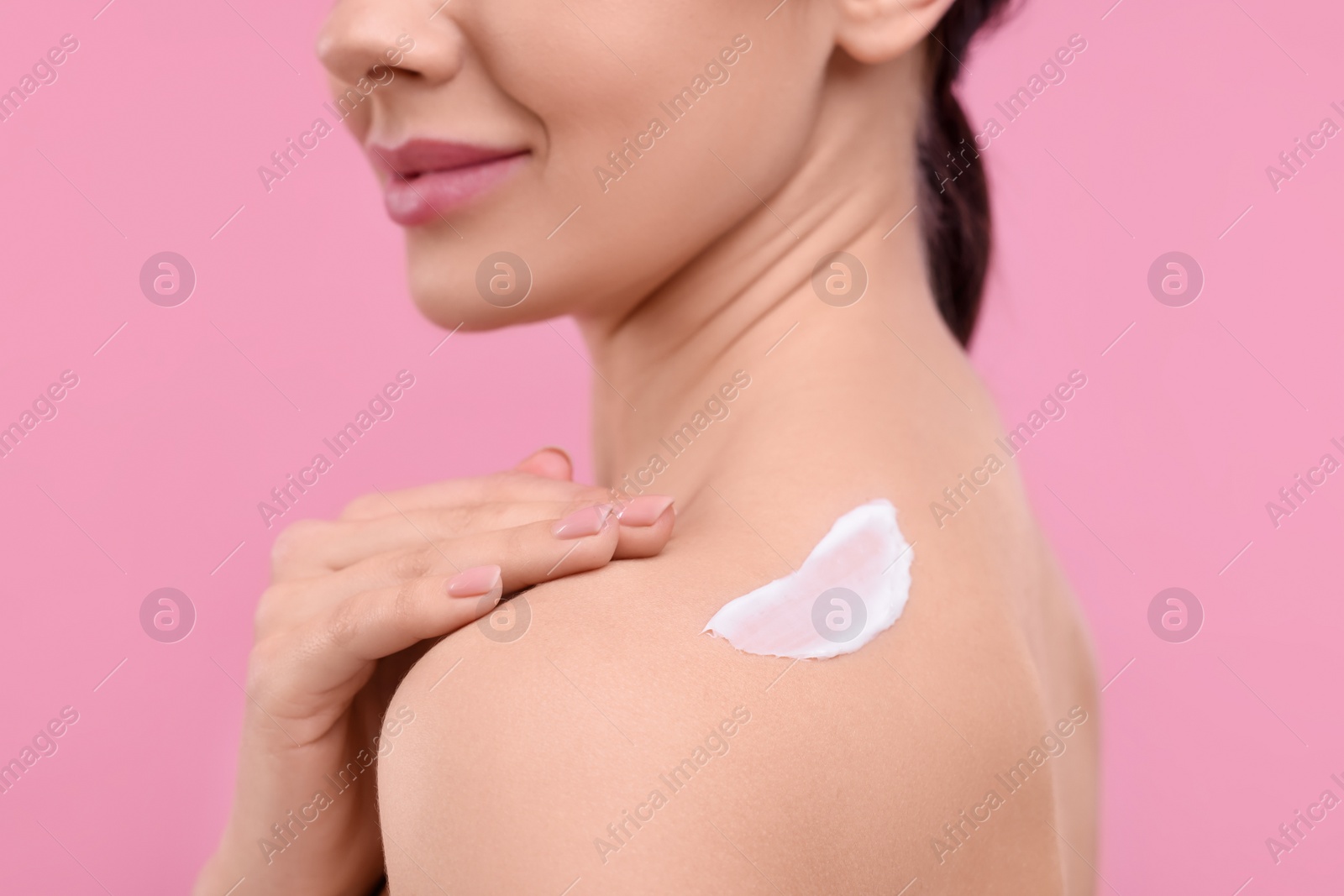 Photo of Woman with smear of body cream on her shoulder against pink background, closeup