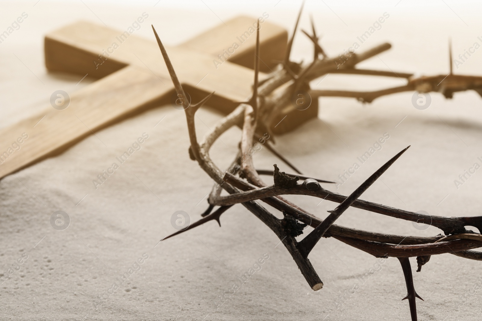 Photo of Crown of thorns and wooden cross on sand, closeup. Easter attributes