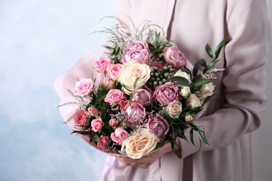 Woman with bouquet of beautiful roses on light blue background, closeup