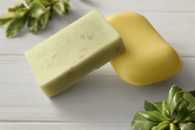 Soap bars and green plants on white wooden table, closeup