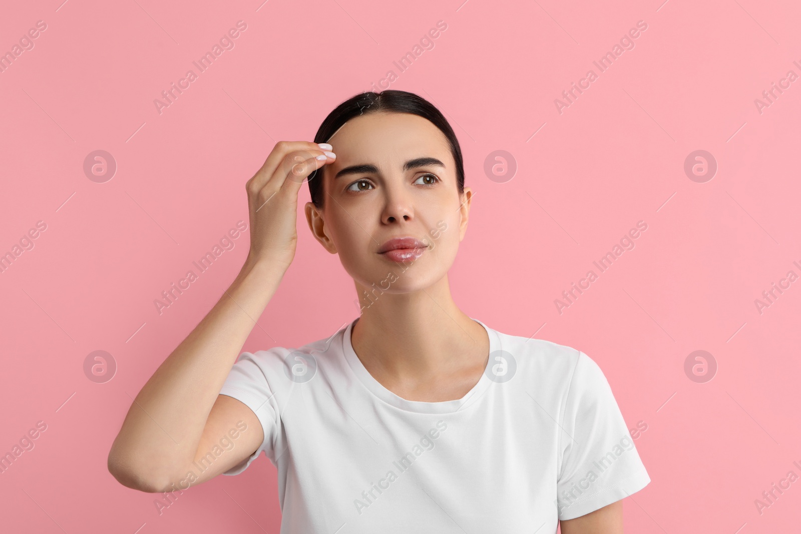 Photo of Woman with dry skin checking her face on pink background
