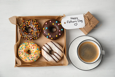 Photo of Tag with phrase HAPPY FATHER'S DAY, donuts, coffee and gift on white wooden table, flat lay