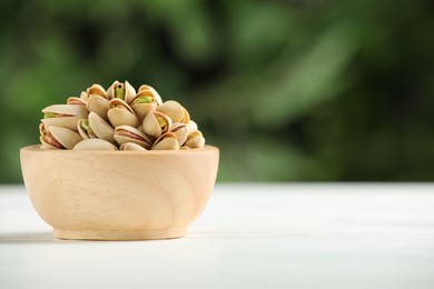 Photo of Tasty pistachios in bowl on white wooden table against blurred background, closeup. Space for text