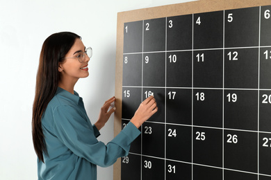 Photo of Young woman writing with chalk on board calendar