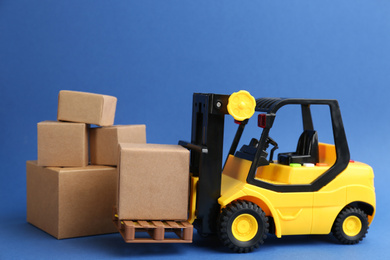 Photo of Forklift model and carton boxes on blue background. Courier service