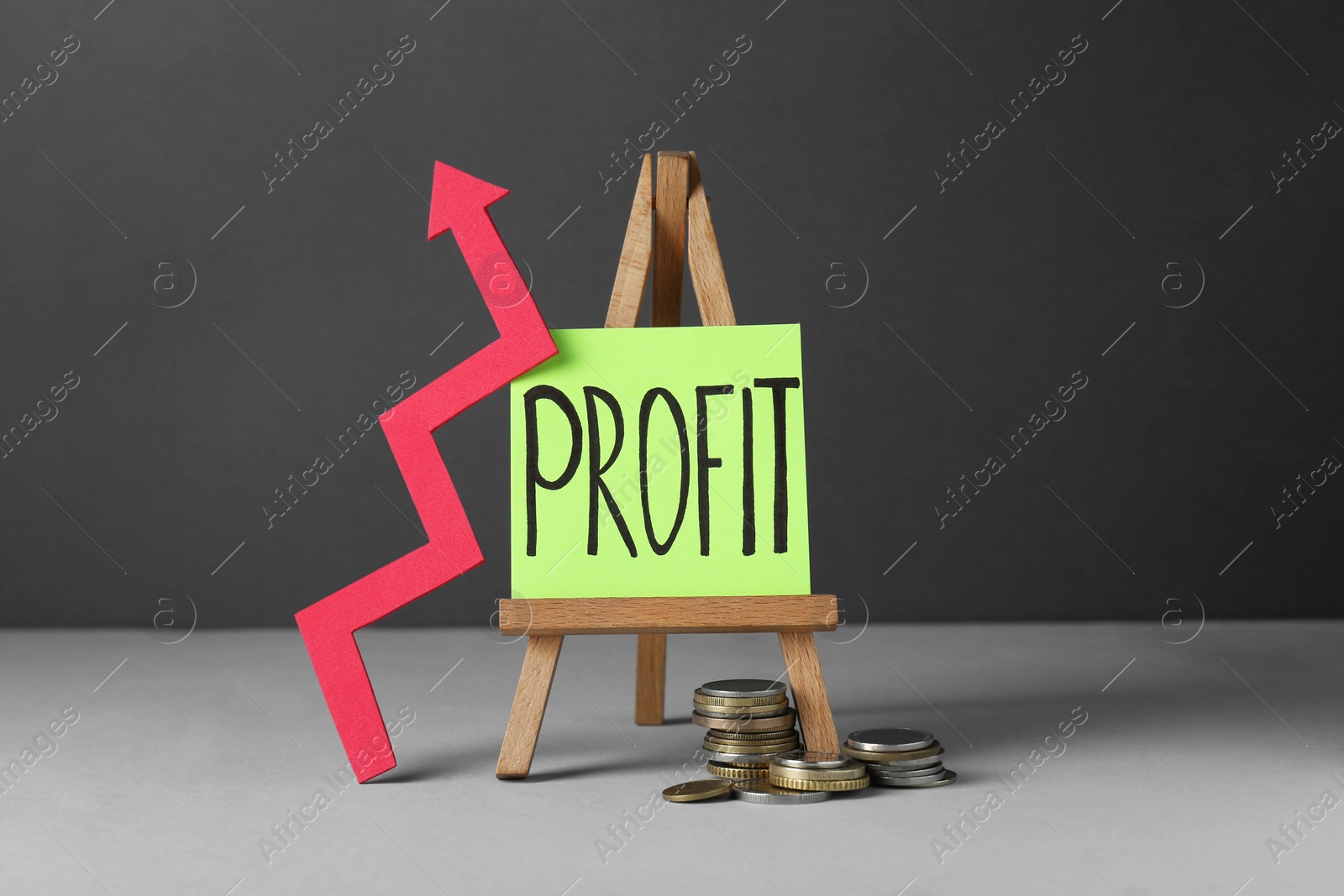 Photo of Economic profit. Arrow, coins and easel with note on grey table