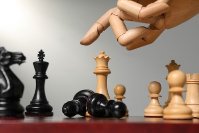 Photo of Robot moving chess piece on board against light grey background, closeup. Wooden hand representing artificial intelligence