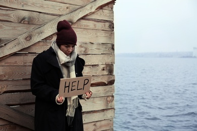 Photo of Poor young woman with HELP sign at riverside. Space for text