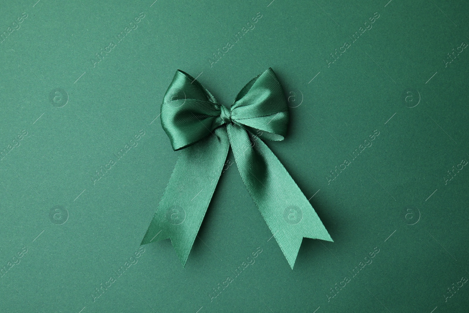 Photo of Bright satin ribbon bow on green background, top view