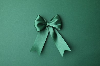 Photo of Bright satin ribbon bow on green background, top view