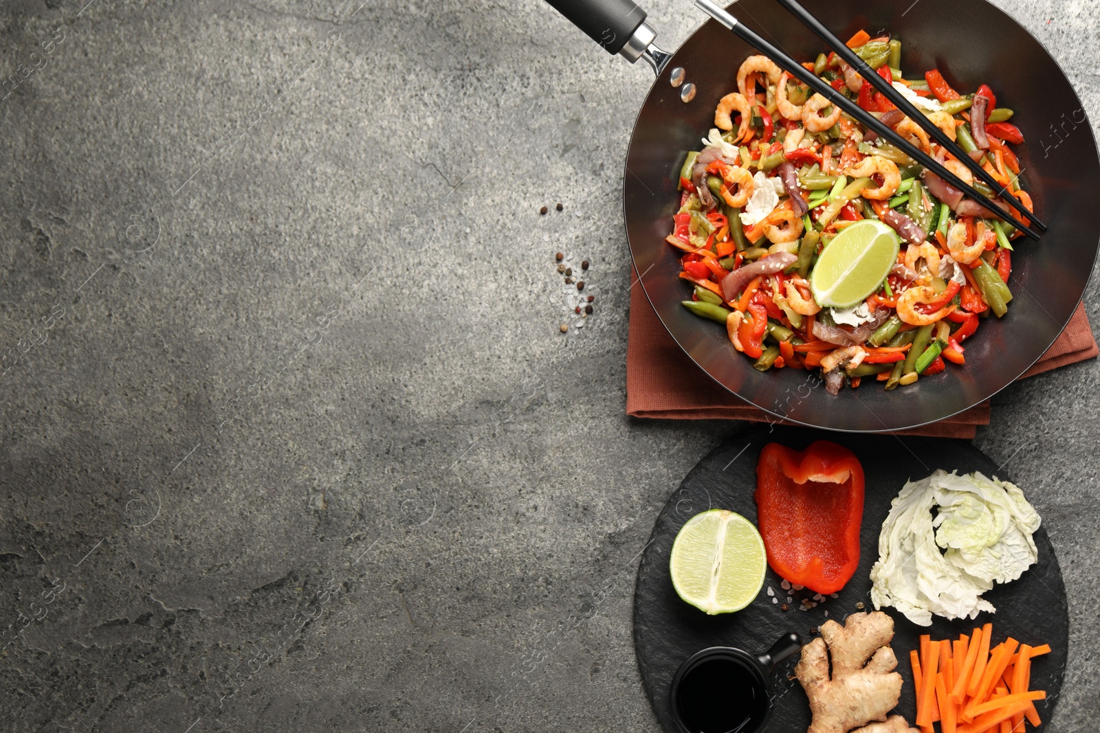 Photo of Shrimp stir fry with vegetables in wok and chopsticks on grey table, flat lay. Space for text