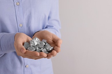 Woman with silver nuggets on light grey background, closeup. Space for text