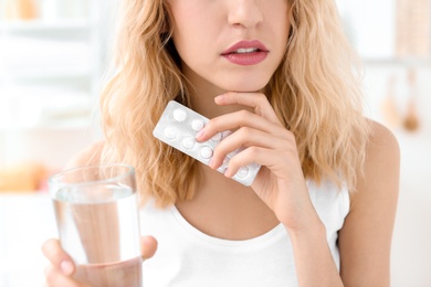 Photo of Young woman with pills and glass of water indoors