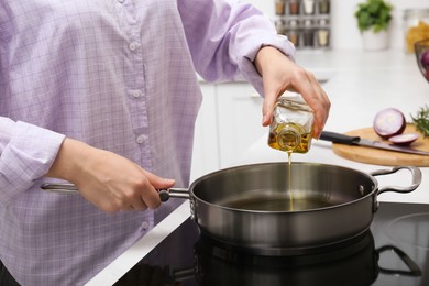 Woman pouring aromatic cooking oil from bottle into frying pan in kitchen, closeup