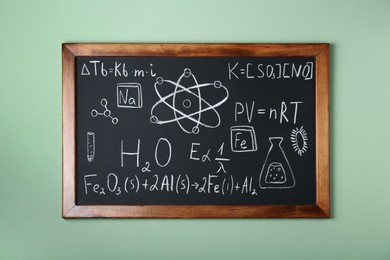 Photo of Blackboard with different chemical formulas written with chalk on light green wall