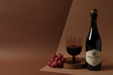 Photo of Delicious red wine and grapes on brown background, space for text