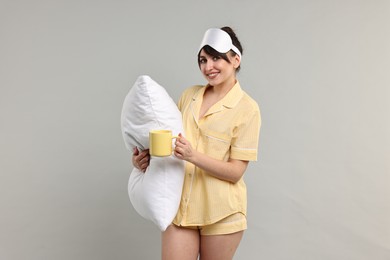 Photo of Happy woman in pyjama holding pillow and cup of drink on grey background