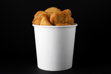 Photo of Bucket with delicious chicken nuggets on black background
