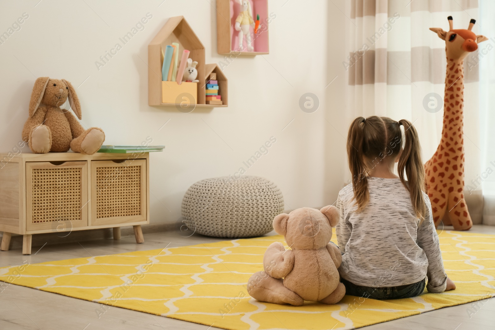 Photo of Lonely little girl with teddy bear sitting on floor at home, back view. Autism concept