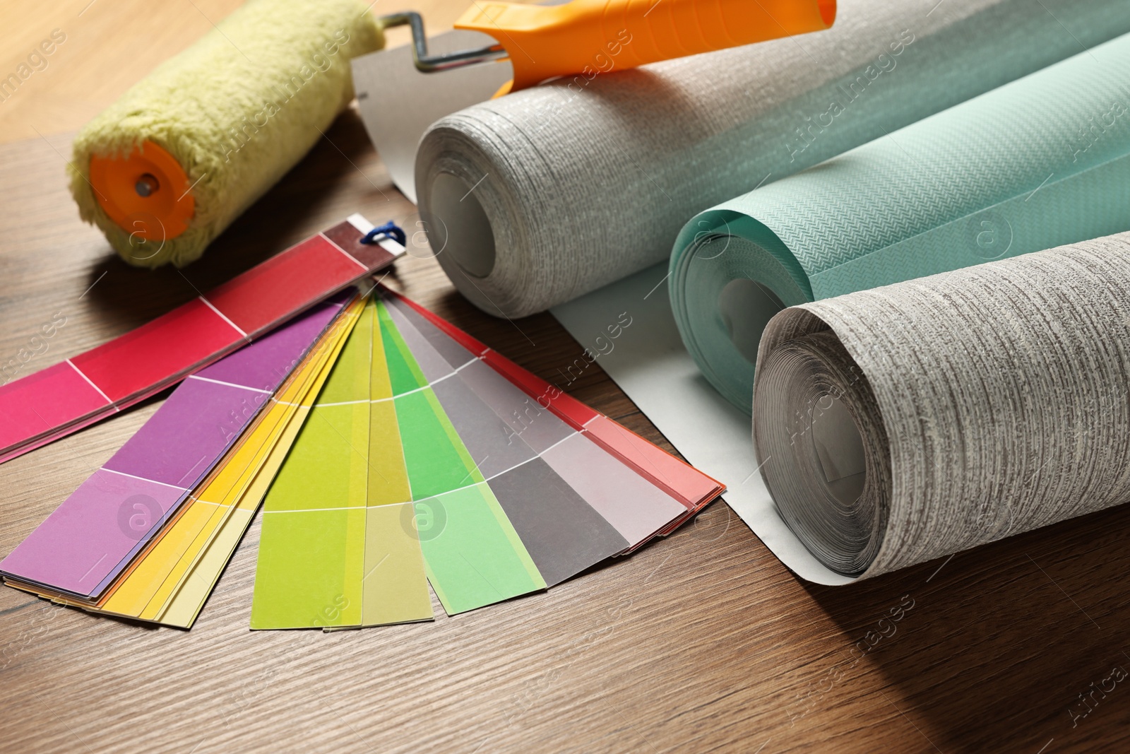 Photo of Different wallpaper rolls, roller and color palette samples on wooden table