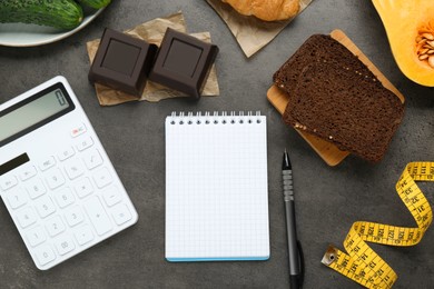 Photo of Food products, notebook with calculator on dark grey table, flat lay. Weight loss and calorie counting concept