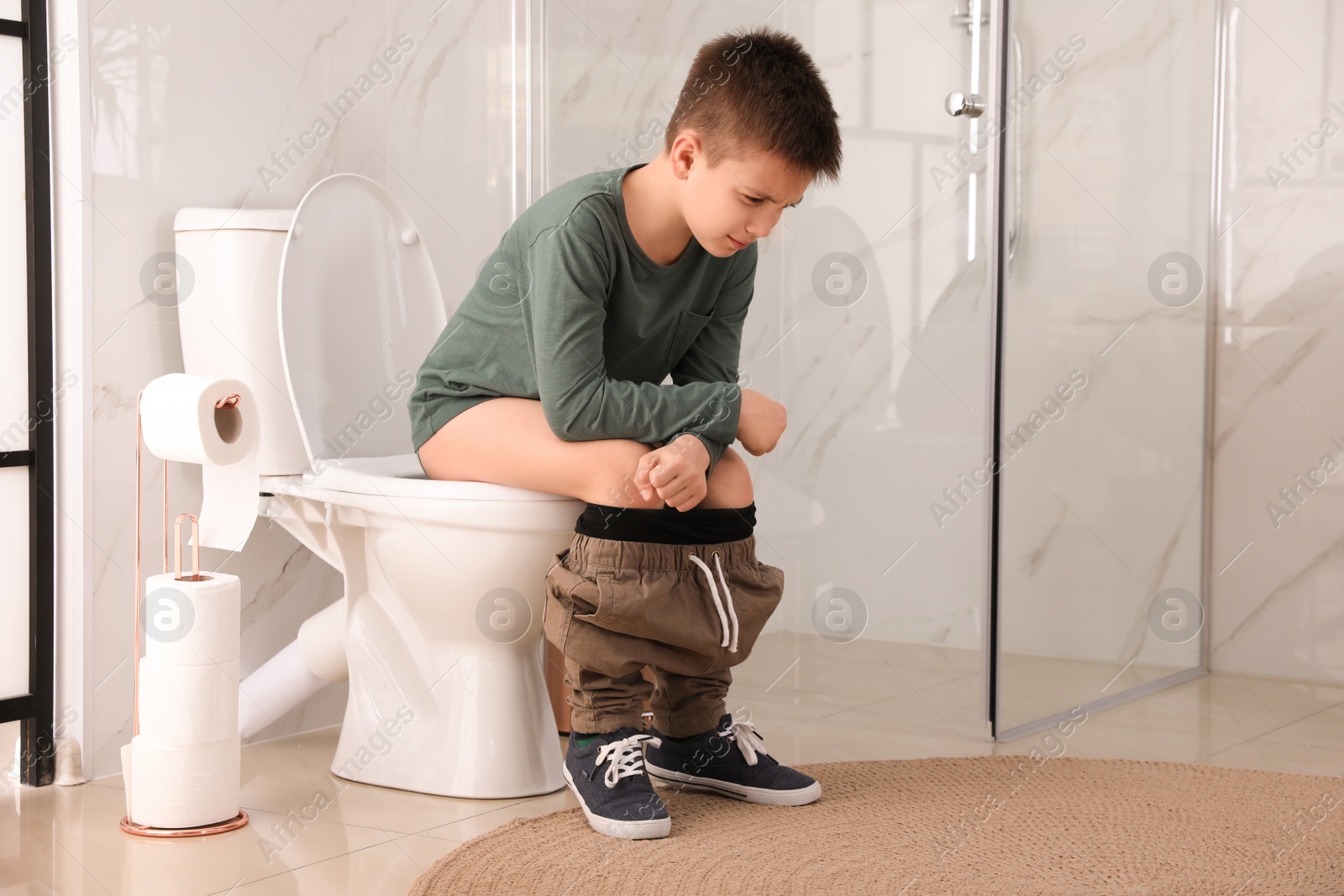 Photo of Boy suffering from hemorrhoid on toilet bowl in rest room