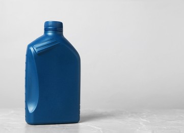 Motor oil in blue canister on grey marble table against light background, space for text