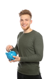 Young man putting money into piggy bank on white background