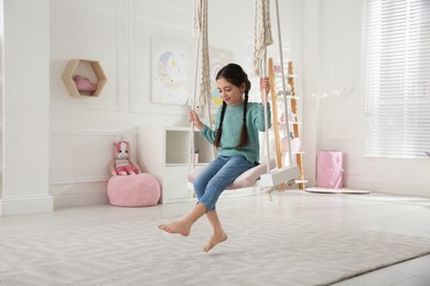 Cute little girl playing on swing at home