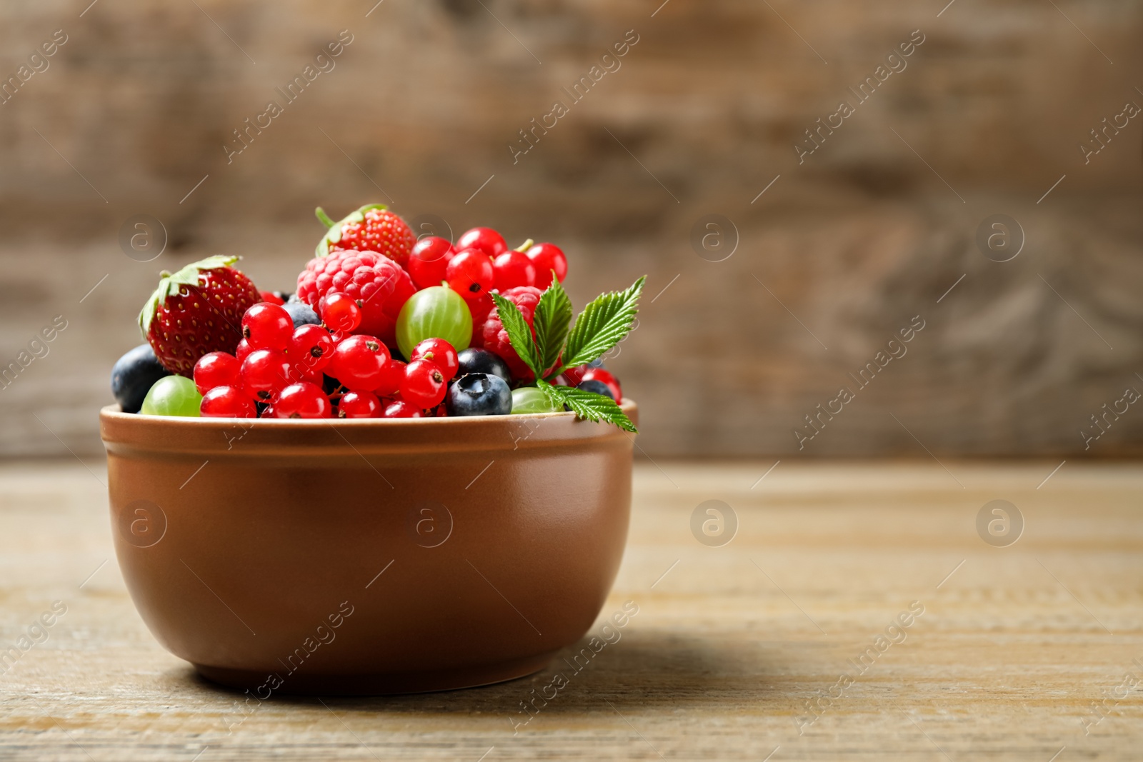 Photo of Mix of different fresh berries in bowl on wooden table. Space for text