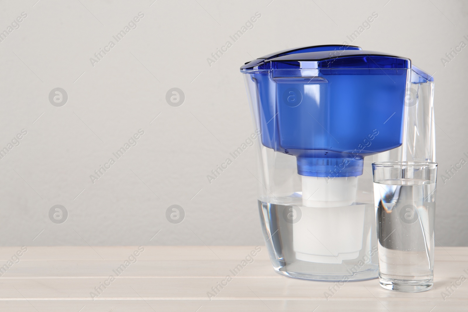 Photo of Filter jug and glass with purified water on white table against light background. Space for text