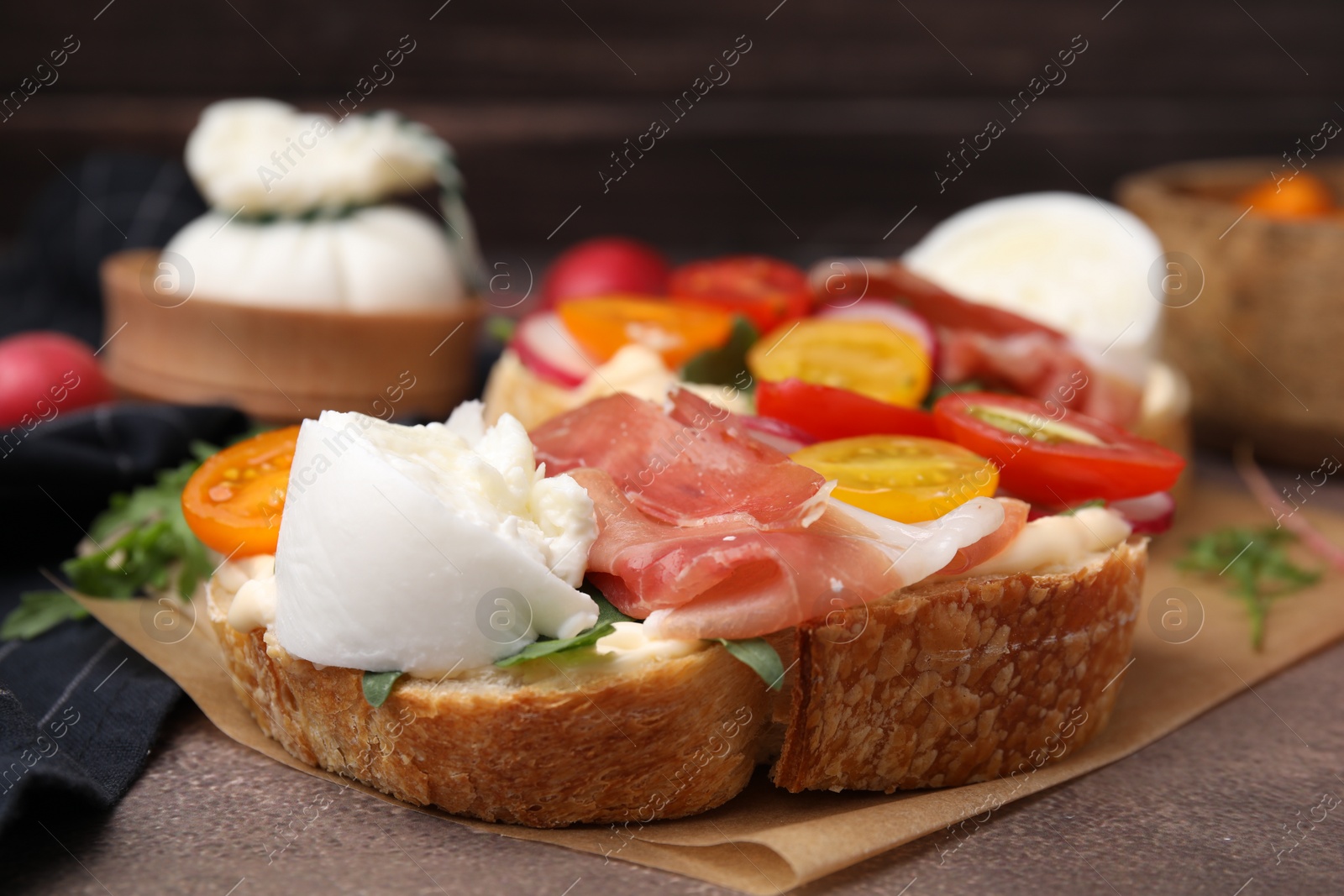 Photo of Delicious sandwich with burrata cheese, ham and tomatoes on brown textured table, closeup