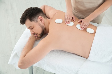 Handsome man receiving hot stone massage in spa salon