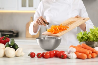 Photo of Professional chef putting cut bell pepper into metal bowl at white marble table in kitchen, closeup