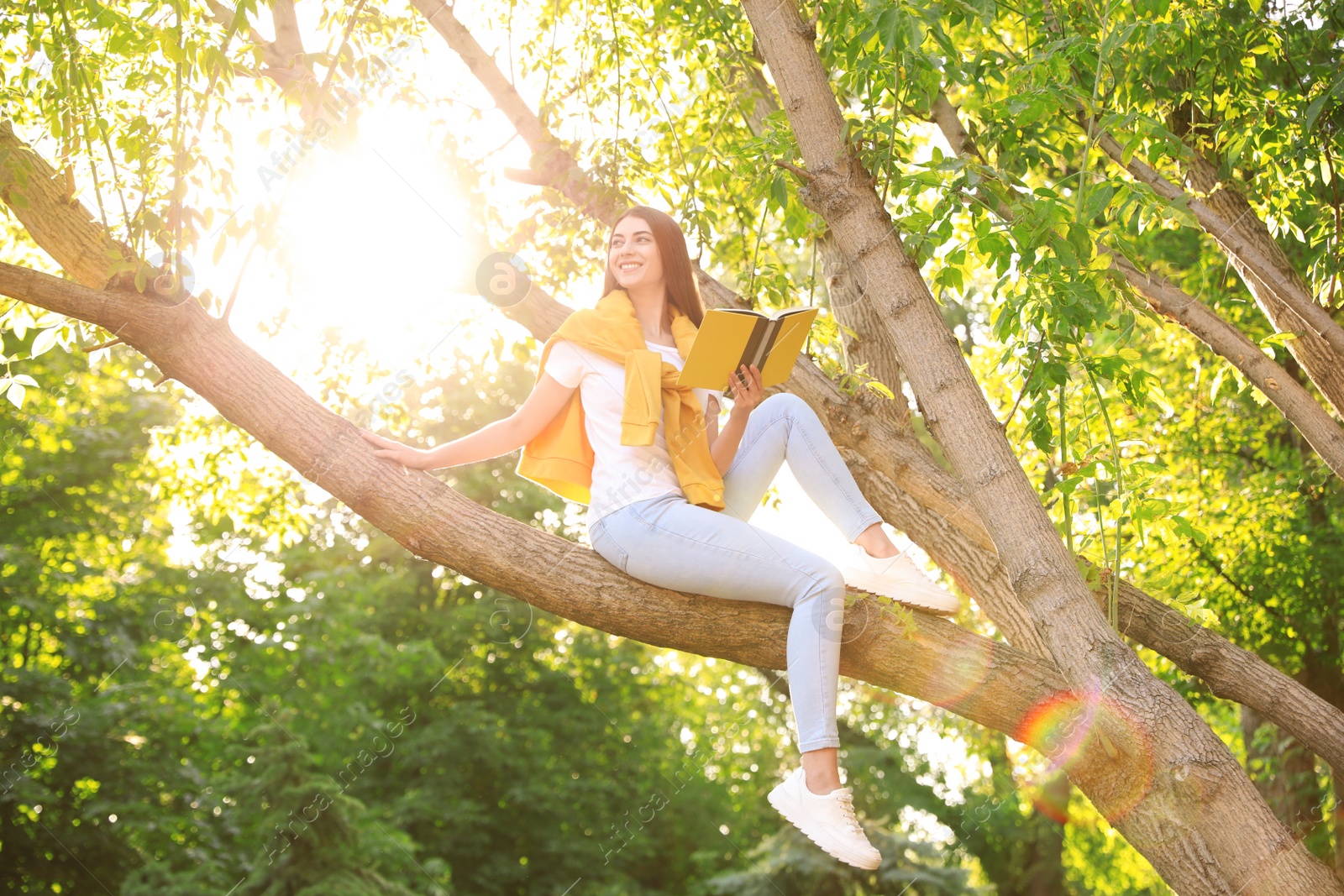 Photo of Young woman reading book on tree in park