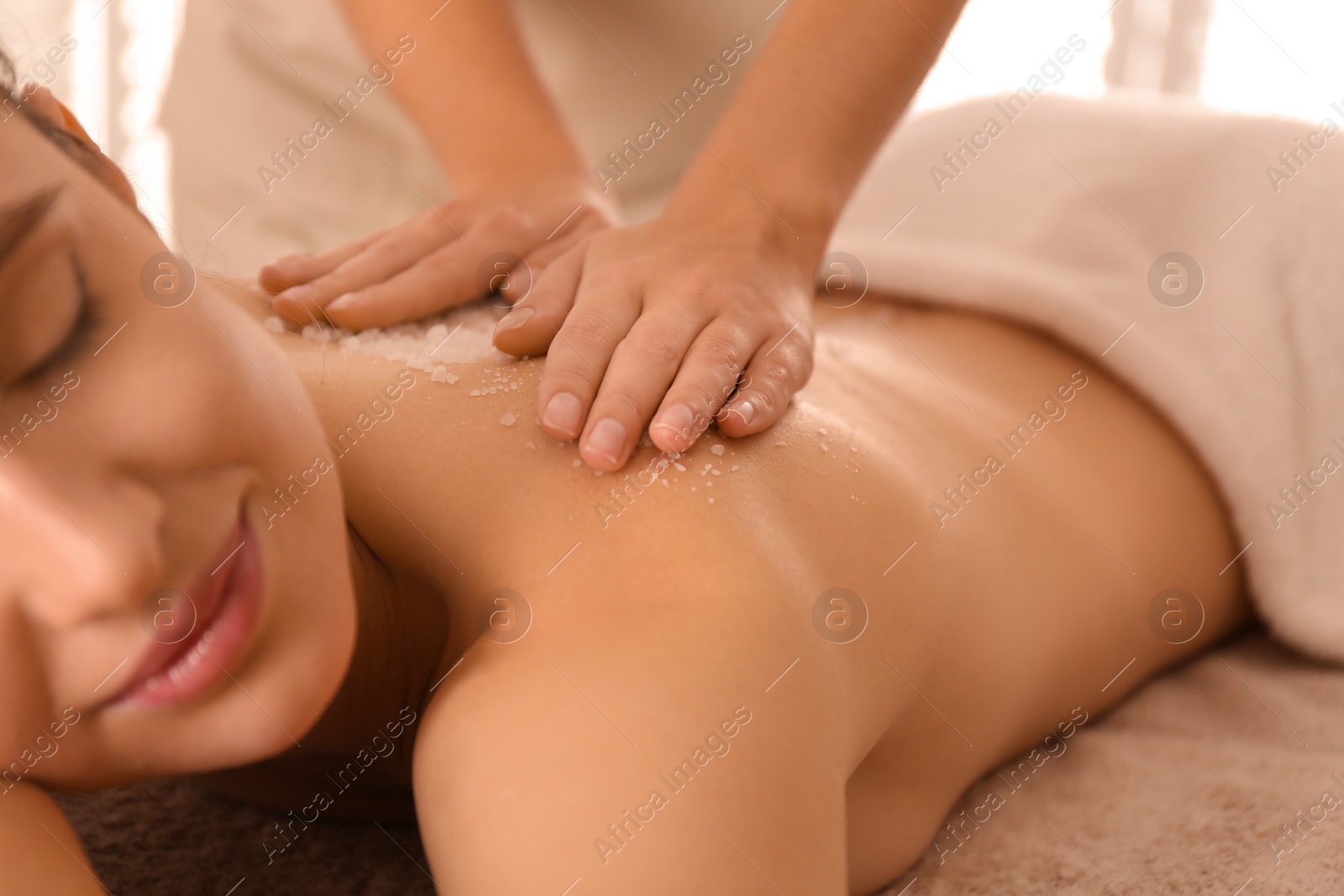 Photo of Young woman having body scrubbing procedure with sea salt in spa salon