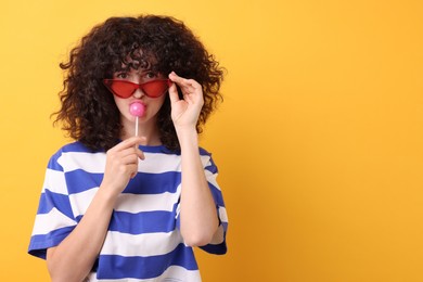 Photo of Beautiful woman in sunglasses with lollipop on yellow background, space for text