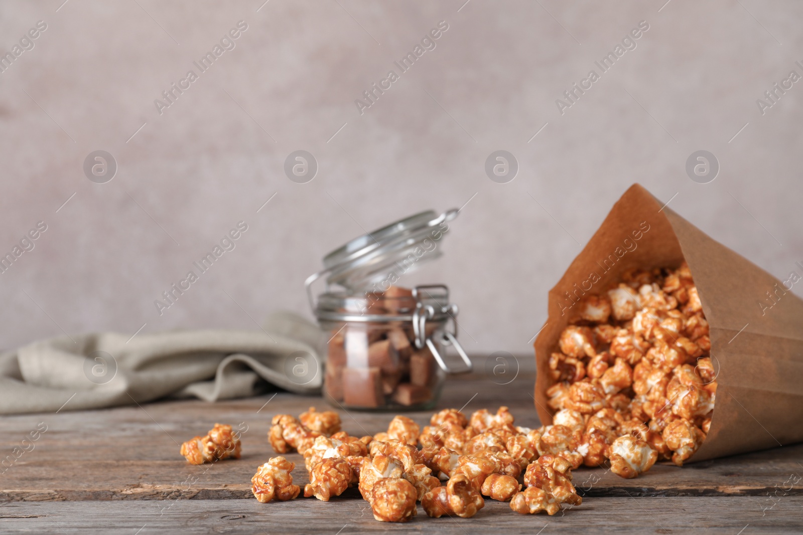 Photo of Overturned paper bag with caramel popcorn on wooden table. Space for text