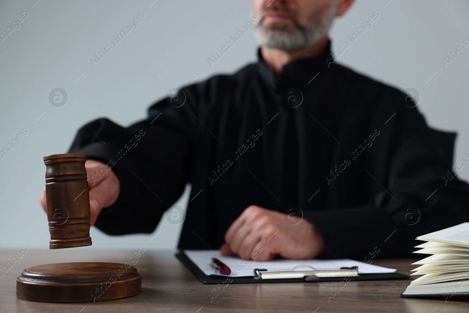 Photo of Judge with gavel and papers sitting at wooden table against light grey background, closeup