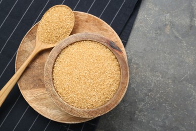 Brown sugar in bowl and spoon on grey textured table, top view. Space for text