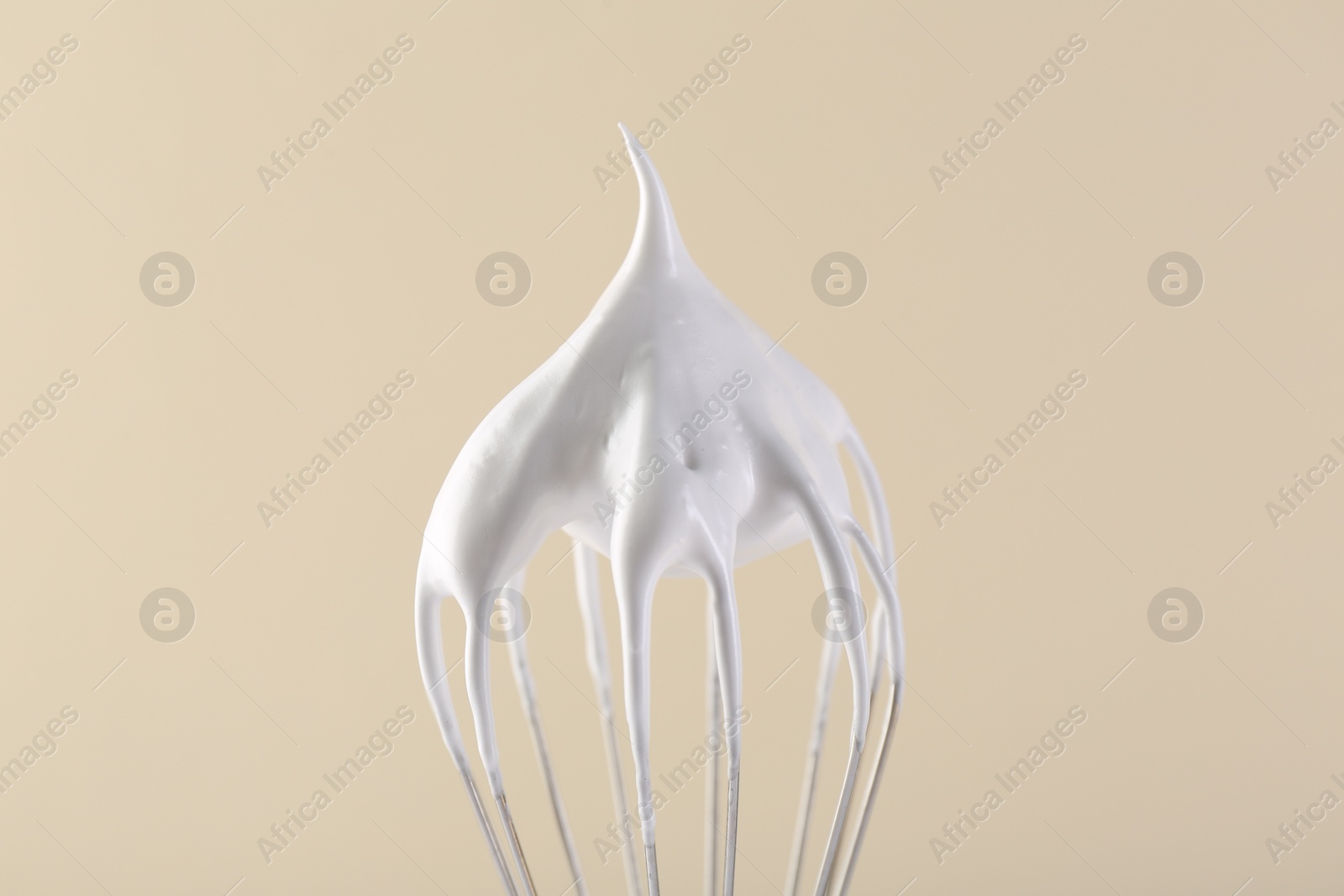 Photo of Whisk with whipped cream on beige background, closeup