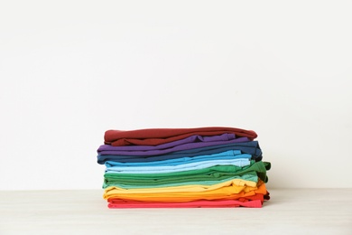 Photo of Stack of bright folded clothes on table against white background. Space for text